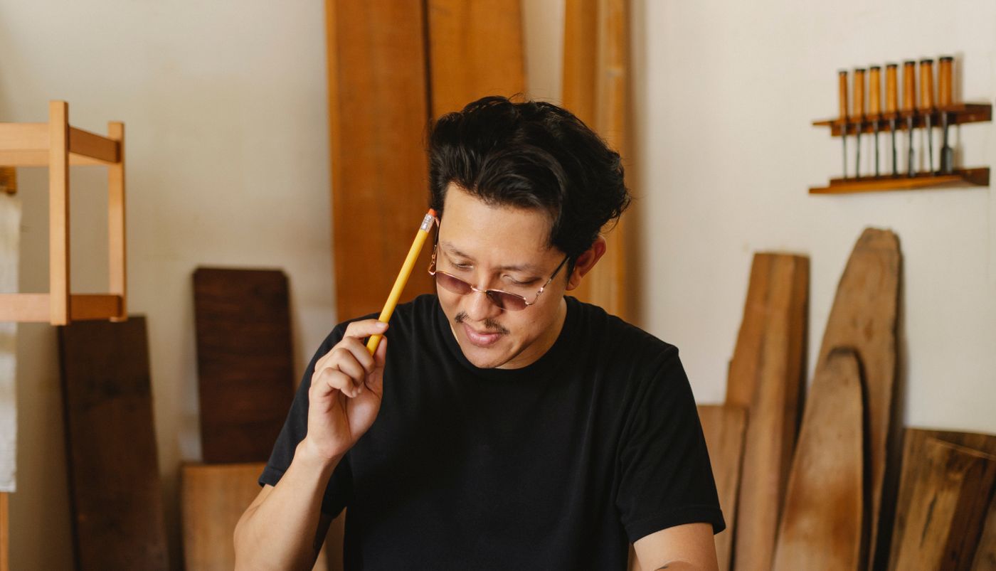 工房で木材を確認するアジア人職人のイメージ